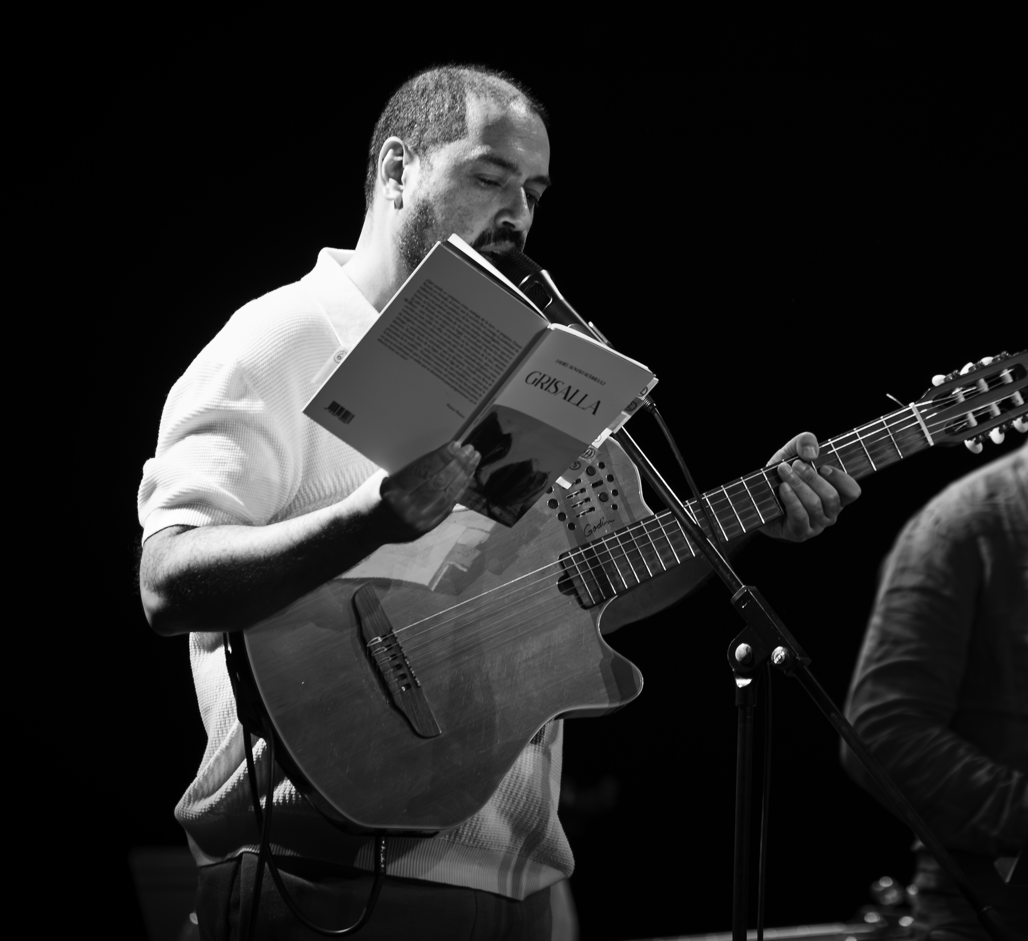 Daniel Román reading poetry on stage while holding a guitar
